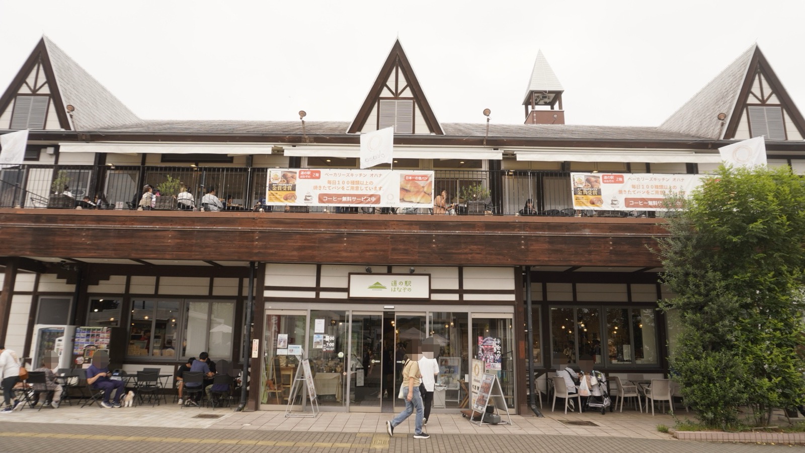 「道の駅 はなぞの」の看板を掲げた、三角屋根が並ぶ2階建ての建物。1階の前にテラス席、2階にバルコニー席がある