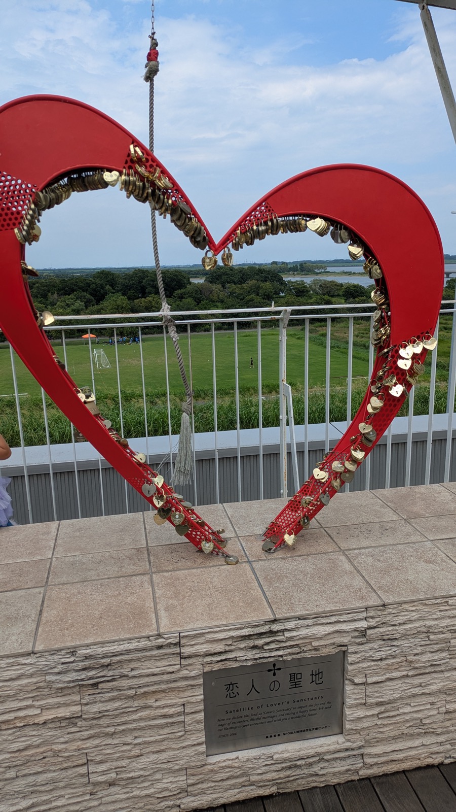 南京錠がびっしりと掛かったハート型のモニュメントと、その向こうに広がる渡良瀬遊水地