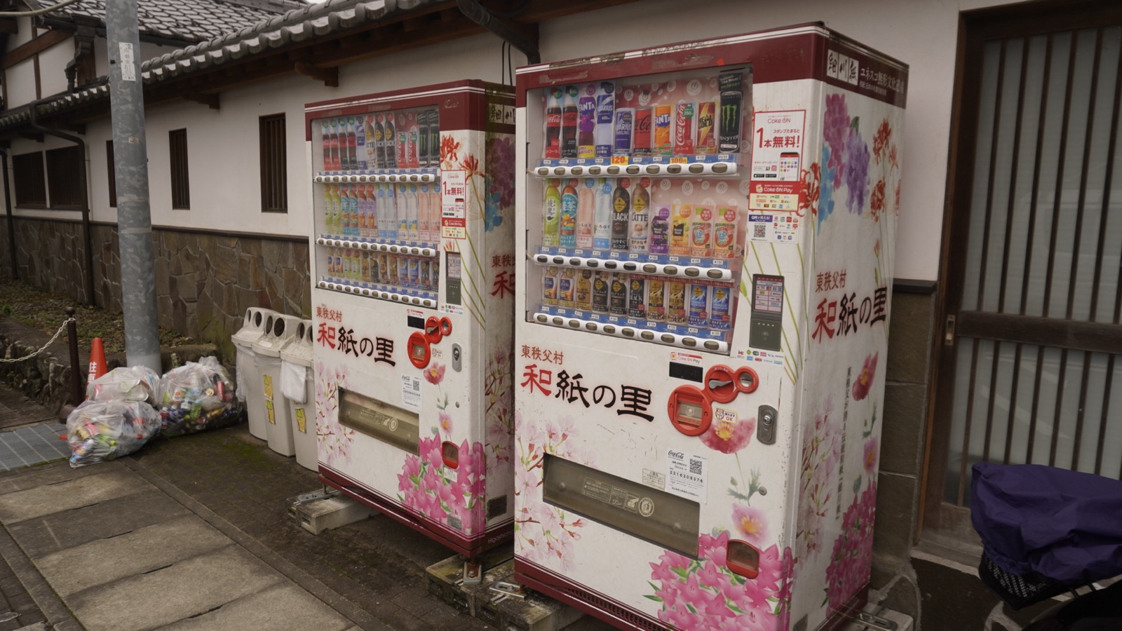白壁の建物の前に2台並んだ自動販売機。白地にピンクの花が描かれ、「東秩父村 和紙の里」の文字が入っている