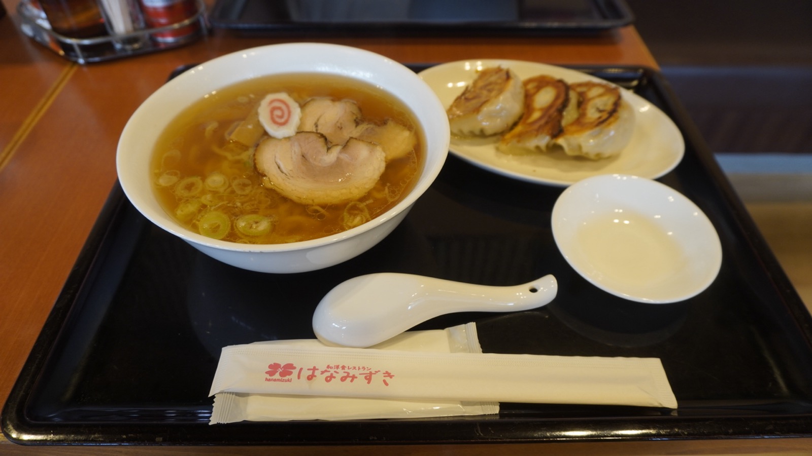 醤油色のスープに縮れ麺、チャーシュー2枚とナルトがのった佐野ラーメンと、焼き餃子3個の皿がのったトレー