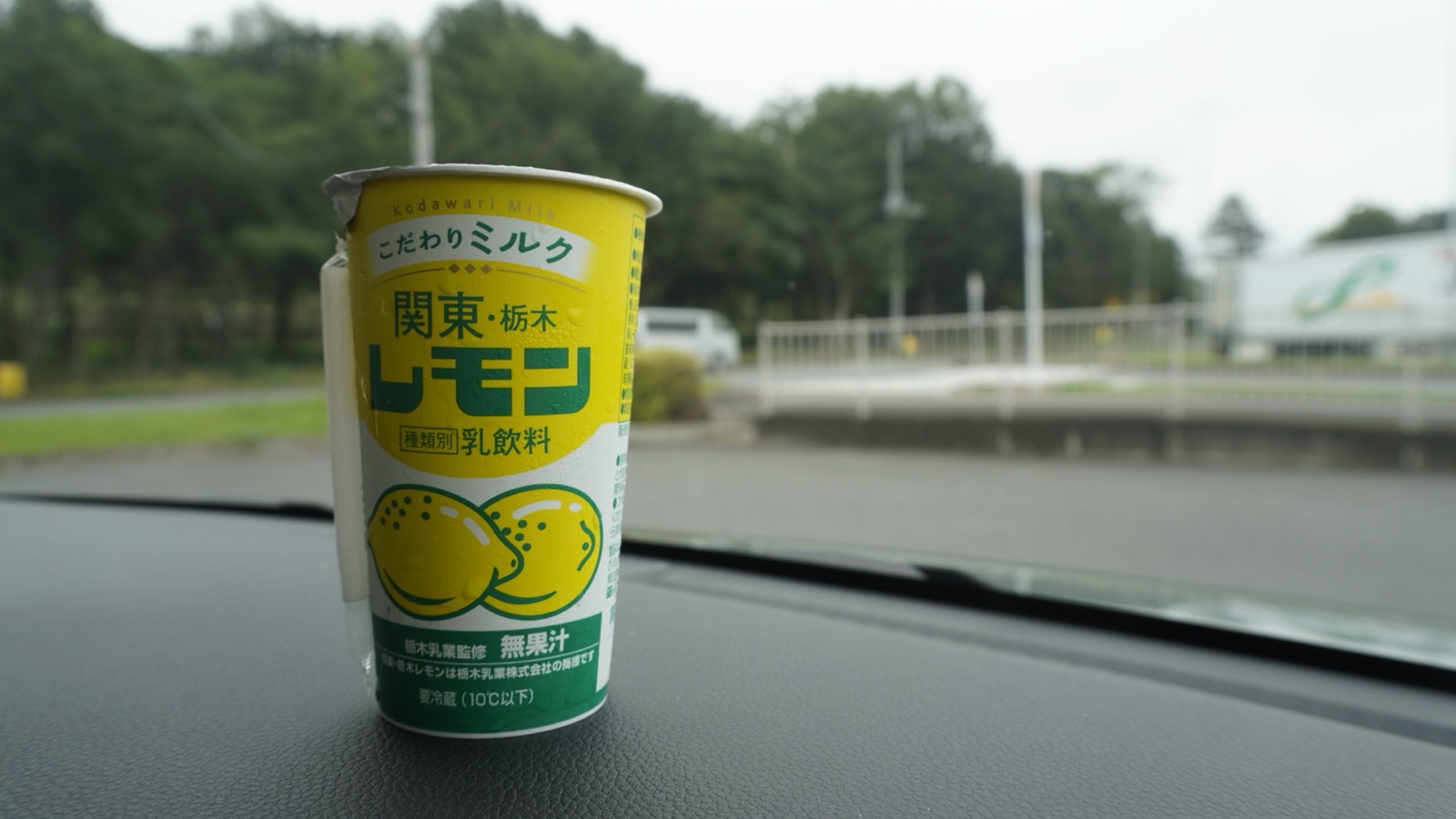 車のダッシュボードに置かれた「関東・栃木レモン」の黄色い紙カップ。フロントガラス越しに駐車場と木々が見える