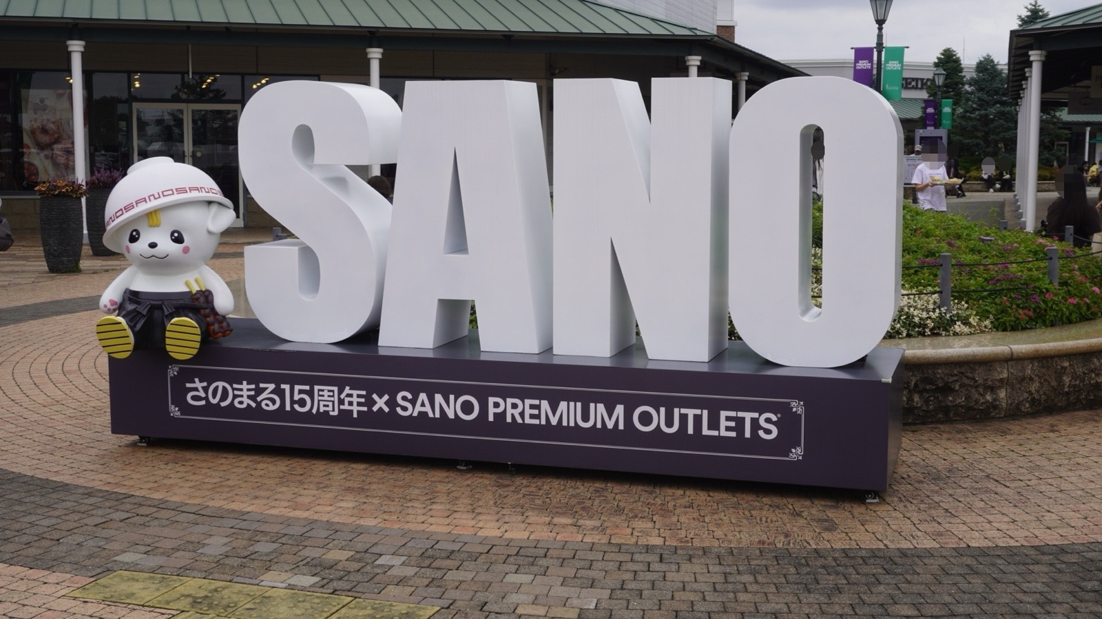 「SANO」の大きな白い立体文字と、その脇に座るさのまるの像。台座に「さのまる15周年×SANO PREMIUM OUTLETS」と書かれている