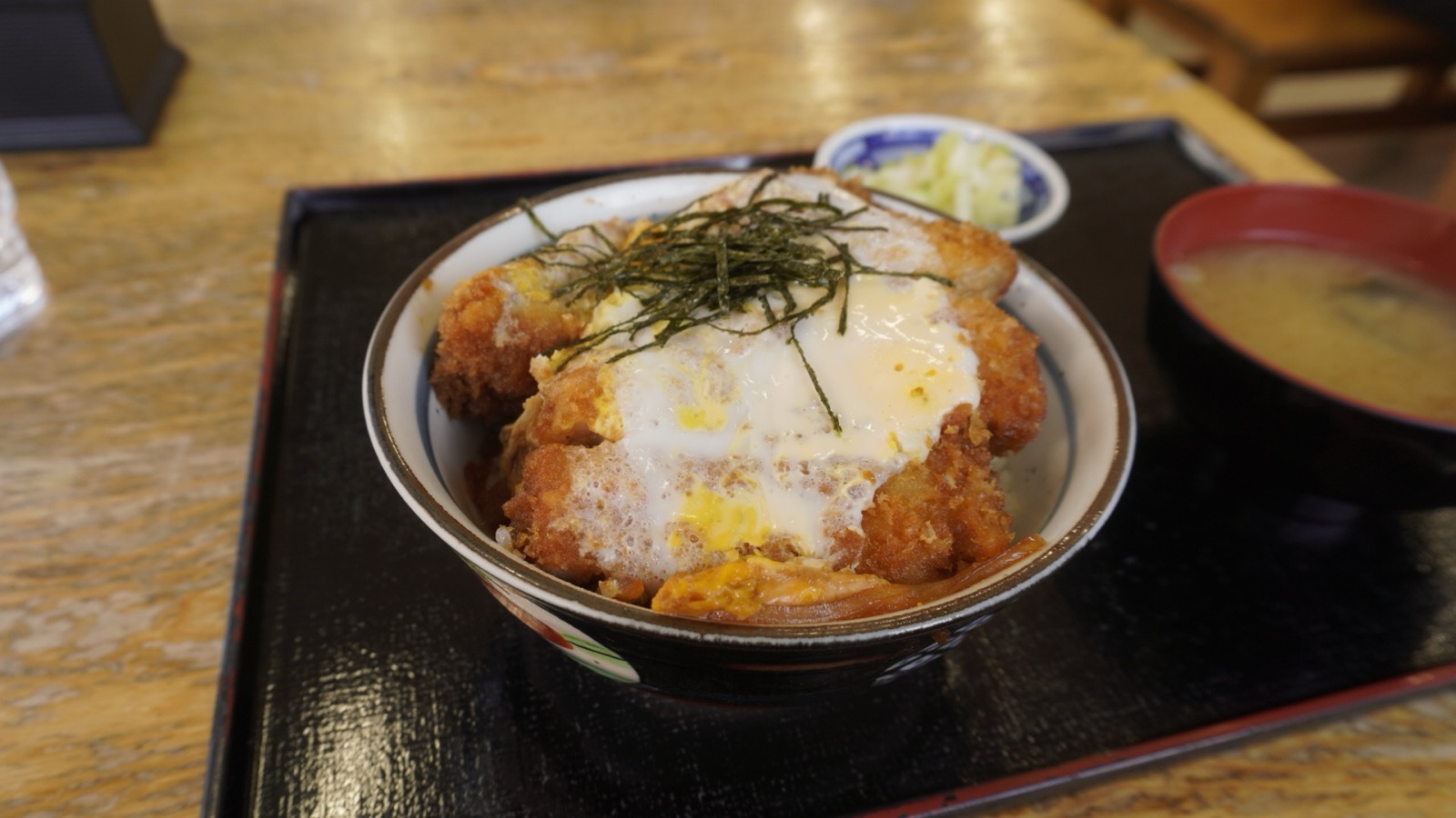 黒い盆にのった海苔と卵とじのかつ丼、みそ汁、漬物