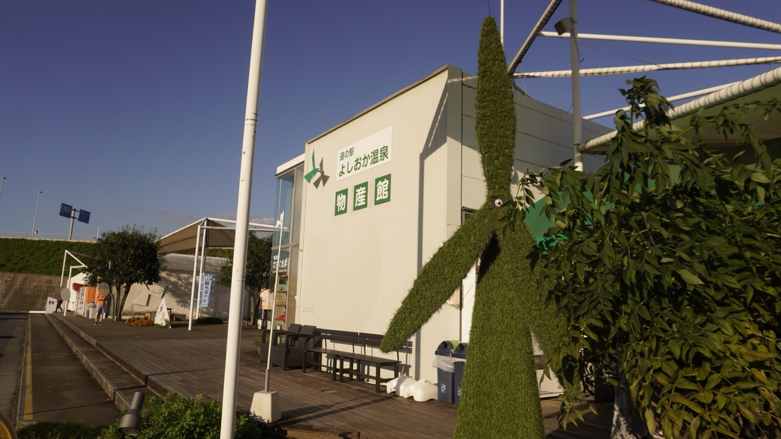 「道の駅 よしおか温泉 物産館」の看板を掲げた建物の前に立つ、芝で覆われた風車のオブジェ