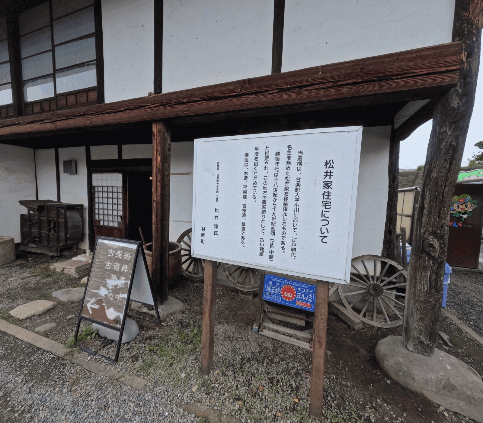 「松井家住宅について」と書かれた説明看板と、その後ろに建つ白壁の古い日本家屋