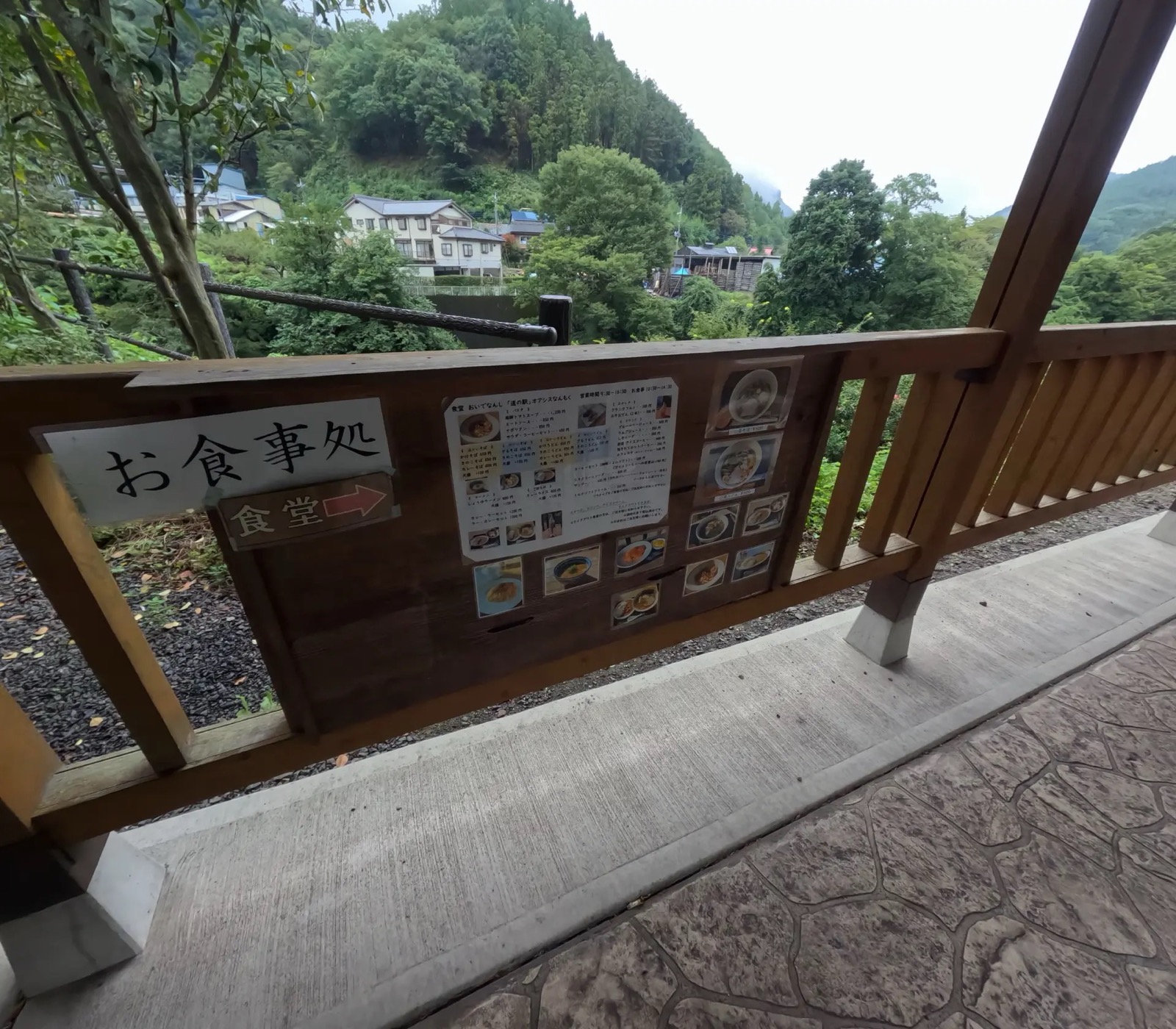 食堂のメニュー表が貼られた木製の柵越しに見える、緑の山と民家