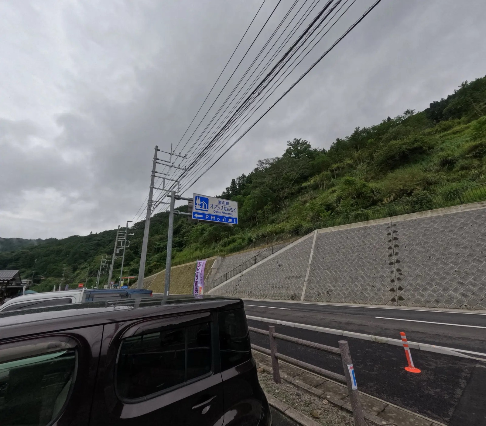 山を背にした「道の駅 オアシスなんもく」の青い案内看板と、駐車中の車列