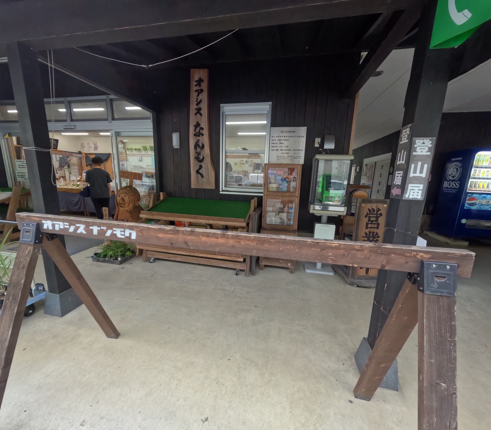 黒い板張りの軒下、「オアシスなんもく」の木彫り看板とベンチ