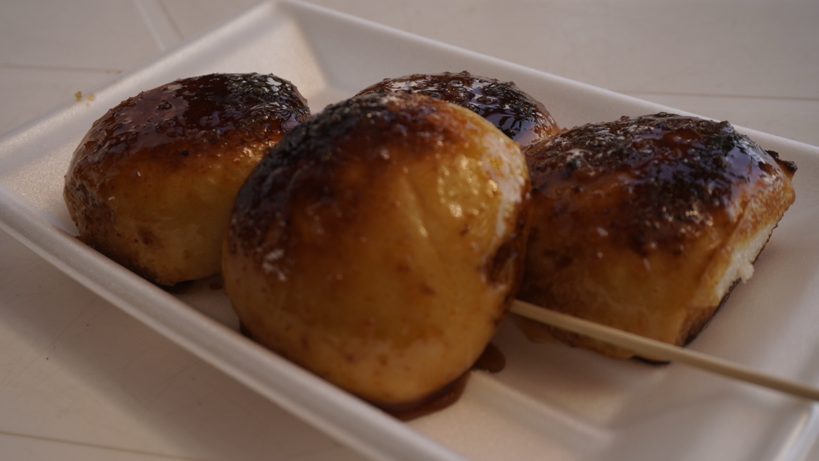 白いトレーにのった串刺しの焼きまんじゅう4個。表面にこげ目の付いた味噌だれが塗られている