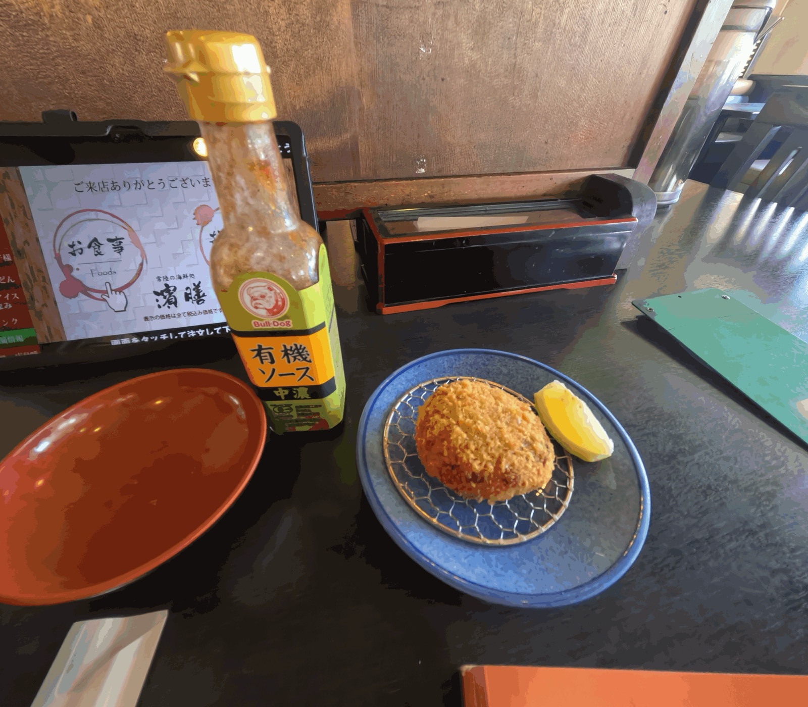 網をのせた青い皿のメンチカツとレモン、横に有機ソースの瓶