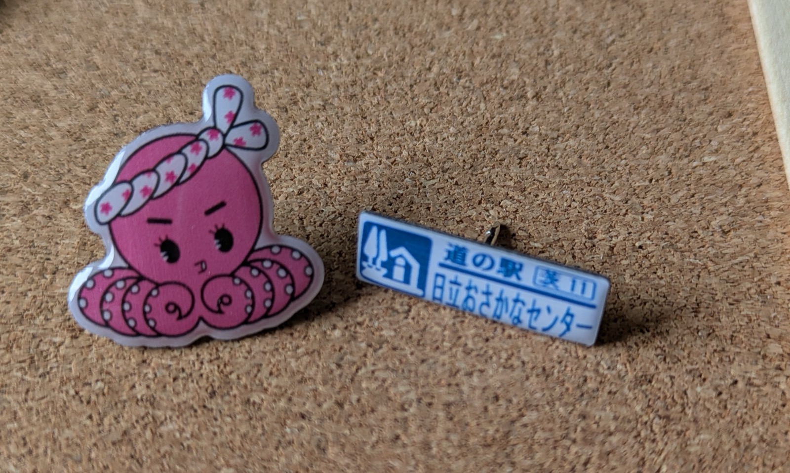 ねじり鉢巻きをしたピンクのタコのピンズと、「道の駅 茨11 日立おさかなセンター」のピンズ