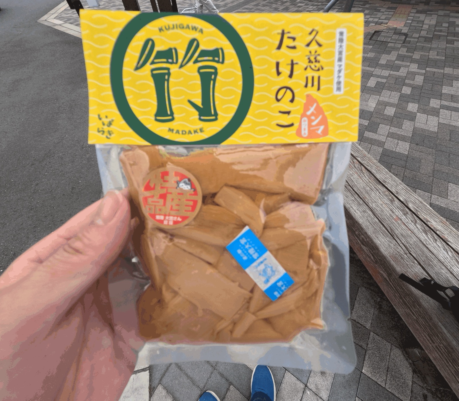 黄色いラベルに「久慈川たけのこ メンマ」と書かれた袋詰めのメンマを手に持った様子