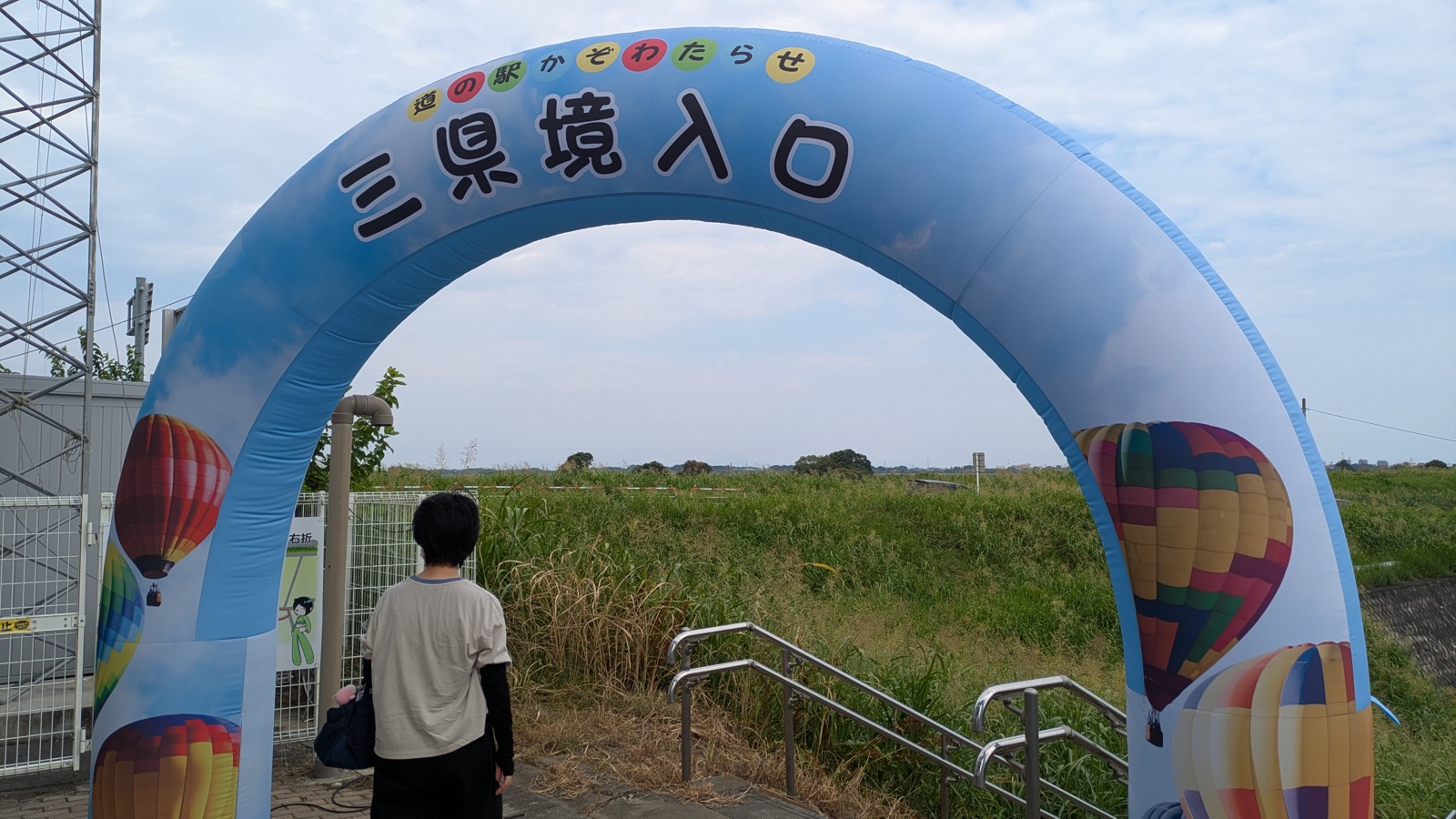 「道の駅かぞわたらせ 三県境入口」と書かれた気球柄のアーチと、その先に広がる草地