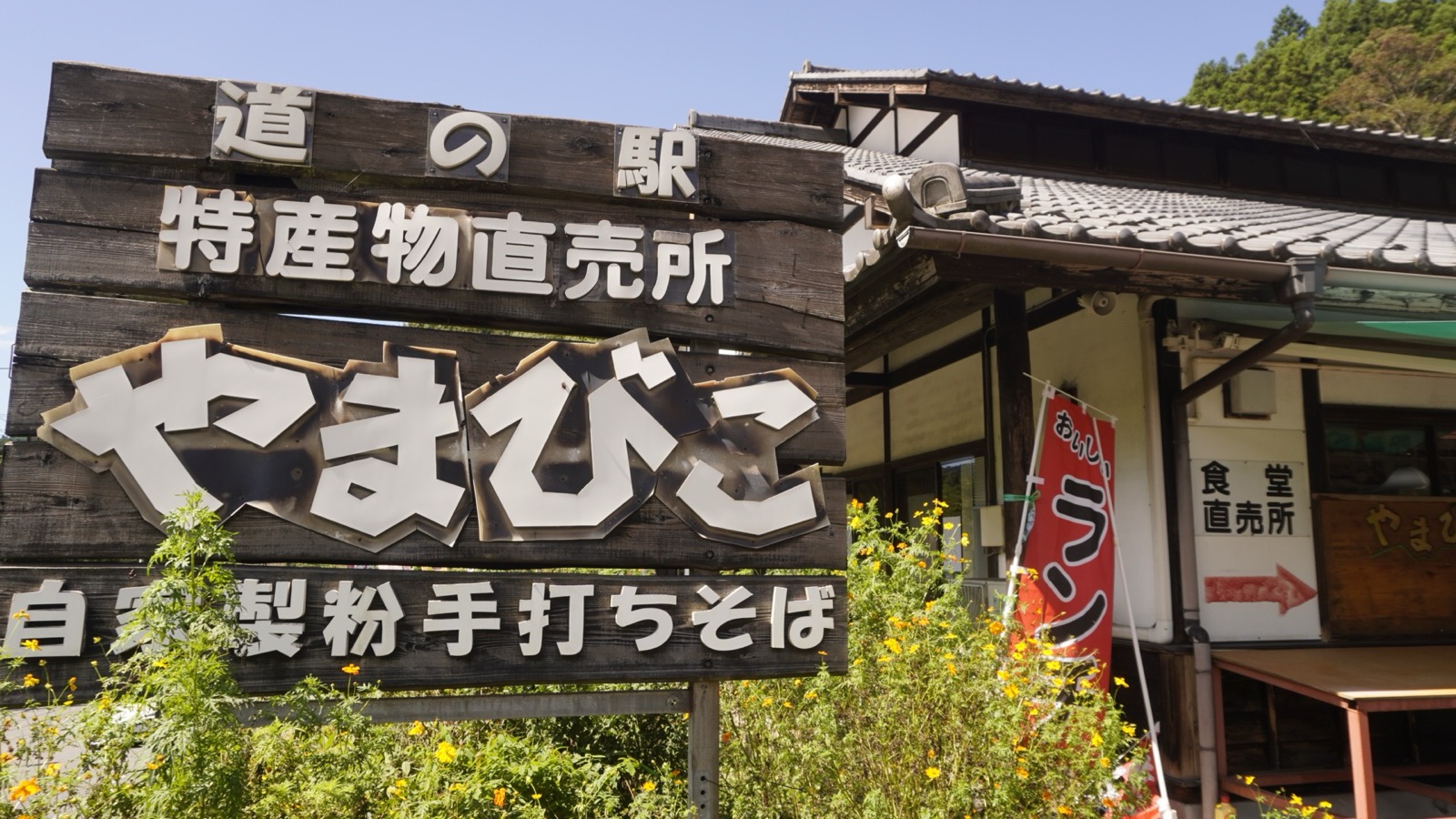 「道の駅 特産物直売所 やまびこ 自家製粉手打ちそば」と書かれた木の看板と、瓦屋根の食堂・直売所の建物