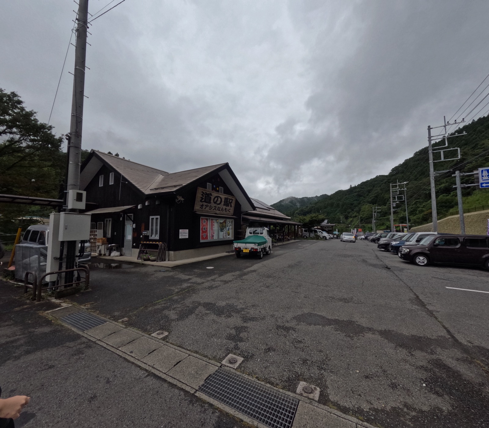 黒い板張りの切妻屋根の建物に「道の駅 オアシスなんもく」の看板が掲げられ、手前に軽トラックと乗用車が並ぶ駐車場が広がる