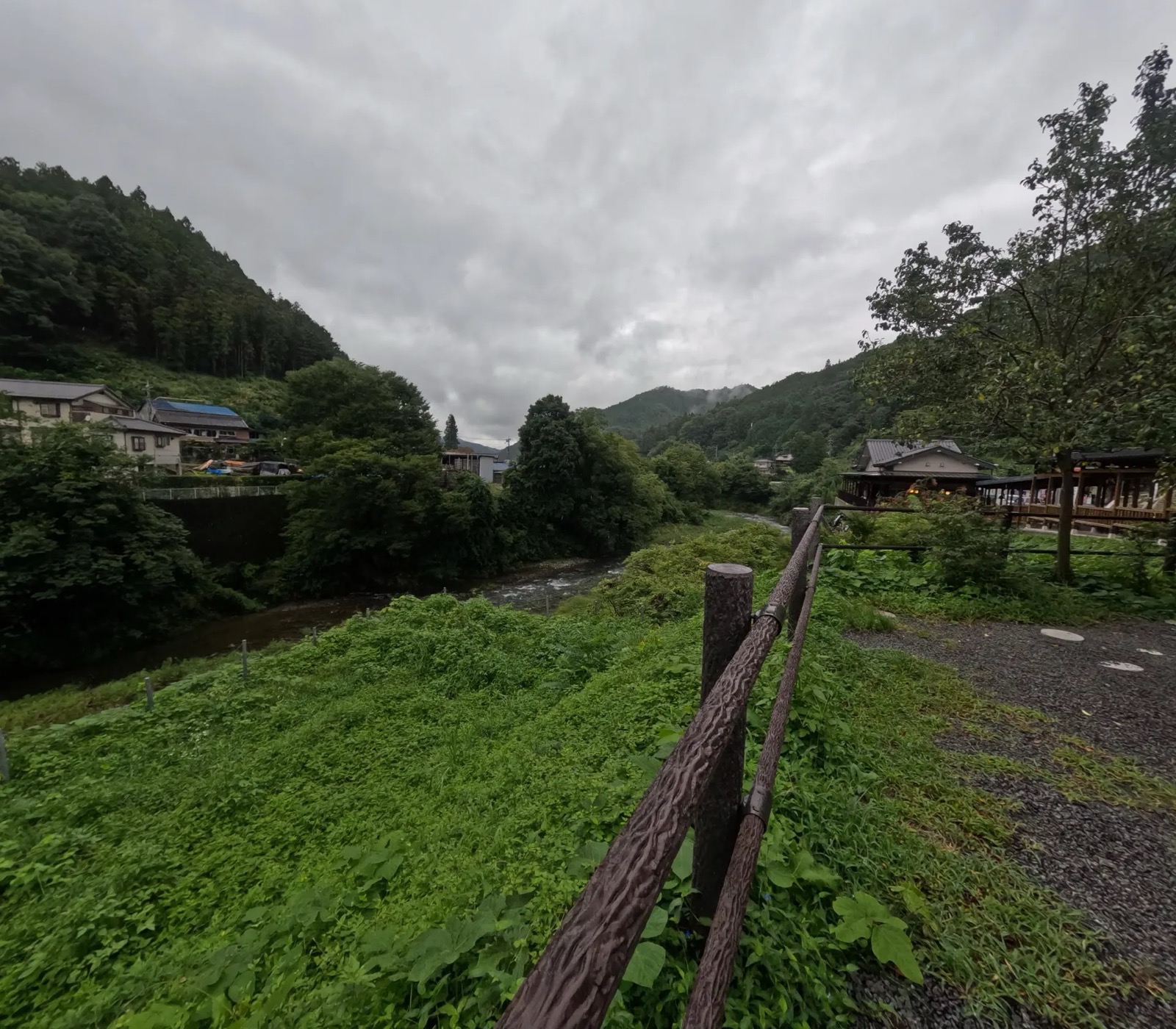 曇り空の下、山あいを流れる南牧川と川沿いの木製の柵