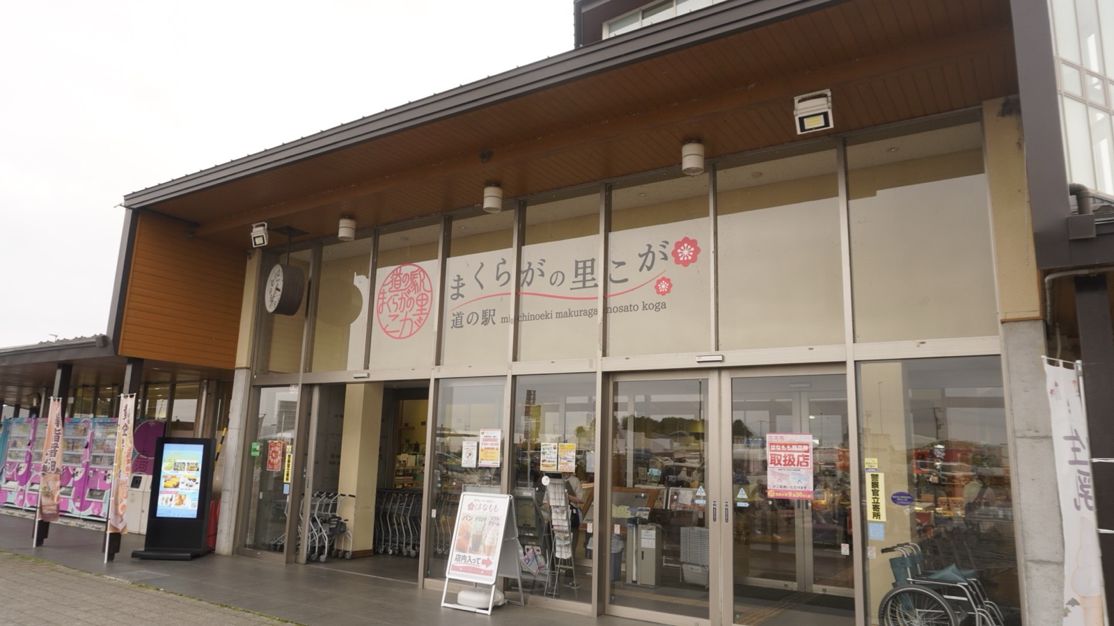 「道の駅 まくらがの里こが」の看板が掲げられた正面入口。自動ドアの前にショッピングカートが並ぶ
