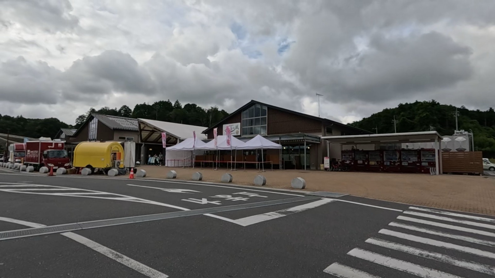 曇り空の下に建つ道の駅かさまの外観。複数の棟が連なる大きな建物で、手前にはテントとキッチンカーが並ぶ